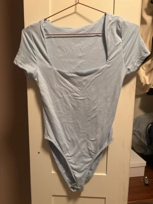 Ljusblå kortärmad body - En enkel och stilren ljusblå body med korta ärmar och fyrkantig ringning. Perfekt att matcha med jeans eller kjol för en clean look. Tillverkad i mjukt stretchigt tyg som sitter skönt mot kroppen.