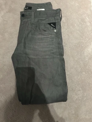 Grå Replay jeans slim fit - Längd 34.                                                  Snygga grå jeans från Replay med klassisk femficksdesign och diskreta sömmar på bakfickorna. Jeansen har slim fit passform och är tillverkade i mjukt bomullsmaterial med lite stretch för extra komfort. Perfekta till en avslappnad stil.