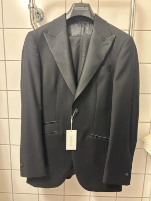 Svart smokingkavaj med satinslag - Klassisk svart smokingkavaj från VOLT och knappar vid ärmsluten. Perfekt för mer uppklädda tillfällen och stilrena outfits. Helt ny och använd med lapp kvar. Nypris 1999kr.