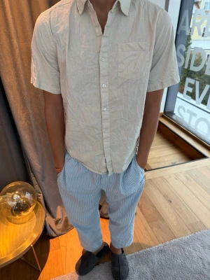 Beige kortärmad linneskjorta - Snygg beige skjorta i linne med korta ärmar och klassisk krage. Skjortan har en bröstficka och knäppning framtill. Perfekt för en avslappnad och stilren look.