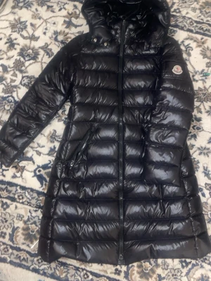Svart Moncler  lång Moka  pufferjacka - I super bra skick! Skickar den på samma eller dagen efter. Den måste säljas akut!