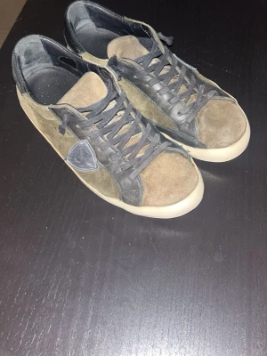 Philippe Model  - Snygga sneakers från Philippe Model i olivgrön mocka med svarta detaljer och vit sula. Skorna har klassisk snörning och en rund tå. Perfekta för dig som gillar en stilren men ändå unik look. Skornas sula har tyvärr släppt i underkanten men super duper lätt att lägga lite lim och trycka, då kommer man inte ens se de, annars är skorna i använt skick men välbevarade.