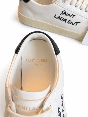 Saint Laurent vita sneakers i skinn - OBS!! Orginalpris 7000kr Mitt pris 1350kr!!! Säljer ett par vita Saint Laurent sneakers i skinn med svart detalj på hälen och handskriven logga på sidan. Klassisk rund tå, vita snören och platt sula. Kommer med originalkartong och kort. Perfekta för dig som gillar stilrena och exklusiva sneakers.