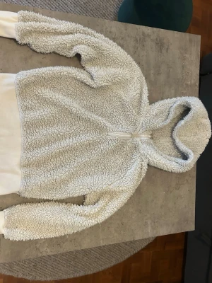 Vit teddyjacka med huva från Etirel - Mysig vit teddyjacka från Etirel i storlek XS. Jackan har huva, half zip-dragkedja och är tillverkad i fluffig fleece som ger en riktigt skön känsla. Perfekt för kyliga dagar och enkel att matcha med det mesta.