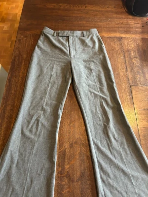 Grå kostymbyxor från Pull&Bear - Snygga grå kostymbyxor från Pull&Bear med klassisk passform och vida ben. Byxorna har hällor för bälte och är tillverkade i ett mjukt material som känns bekvämt hela dagen. Perfekta för en stilren look.