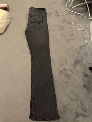 Svarta jeans från Junkyard låg midjad - Säljer ett par svarta  jeans från Junkyard i storlek S. Jeansen har klassisk femficksdesign, bälteshällor och knappgylf. Materialet är mjukt och stretchigt för en bekväm passform. Perfekta till sneakers eller boots.