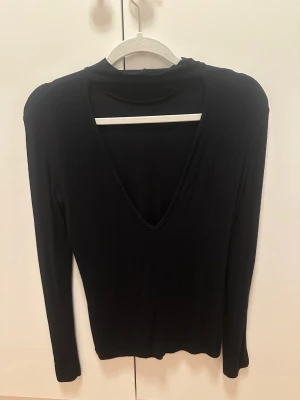 Svart ribbad långärmad topp med v-ringning i ryggen - En svart långärmad topp i mjukt, tunt material med djup v-ringning baktill. Modellen är enkel och stilren med smal passform och utan synliga detaljer. Perfekt att styla med jeans eller kjol för en clean look