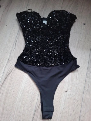 Svart paljett body  - Snygg svart body med glittriga paljetter över hela överdelen och en klassisk sweetheart-ringning. Nedre delen är i slät, lätt stretchig textil för skön passform. Perfekt för dig som vill sticka ut och glänsa lite extra.  Helt ny med lapp passade inte mig så säljer vidare. Från hm
