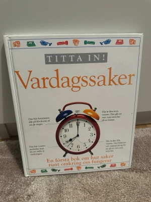 Titta in! Vardagssaker bok - En illustrerad faktabok som förklarar hur olika vardagssaker fungerar. Omslaget är vitt med färgglada illustrationer av saker som väckarklocka, kamera och telefon. Perfekt för dig som är nyfiken på teknik och prylar i hemmet.