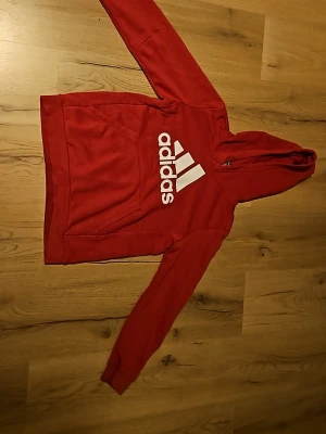 Röd Adidas hoodie med vit logga - Röd hoodie från Adidas med stor vit logga på bröstet och klassisk känguruficka. Tröjan har huva och är gjord i mjukt material, perfekt för en sportig och avslappnad look. Fläkarna är inte lika tydliga längre (gnugade bort med lite vatten) är storlek 150 men sitter typ stl 146. Skriv om ni har frågor eller vill ha fler bilder. Kan discuttera pris.