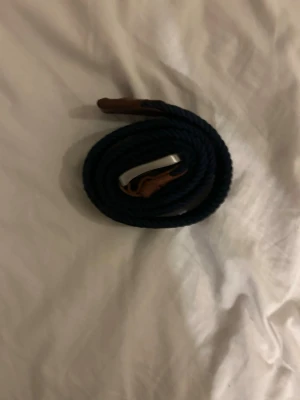 Marinblått flätat bälte med läderdetaljer - Snyggt marinblått flätat bälte från Jack and Jones med bruna läderdetaljer och silverfärgat spänne. Perfekt accessoar för att lyfta din outfit med en klassisk touch. Bältet har en flexibel design tack vare det elastiska materialet.