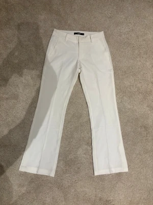 Vita kostymbyxor med raka ben - Stilrena vita kostymbyxor med raka ben, liten slits och pressveck. Byxorna har fickor fram och bak samt klassisk passform. Helt oanvända men utan prislapp!