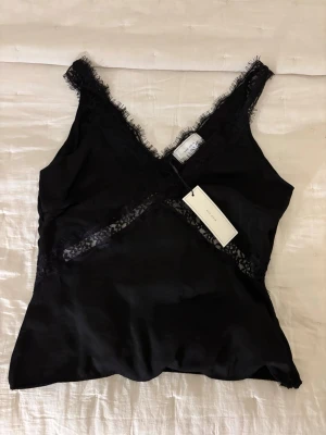 Svart topp med spets  - Svart linnetopp från Neo Noir med spetsdetaljer och glansig yta💕originalpris 599kr, aldrig använd