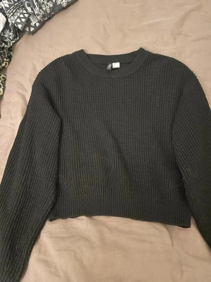 Svart croppad stickad tröja Gina Tricot - Svart croppad stickad tröja från Gina Tricot i storlek S. Tröjan har ribbad struktur, rund hals och långa ärmar. Perfekt för lager-på-lager och passar till både jeans och kjol. Enkel och stilren design som är lätt att matcha.