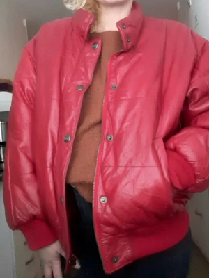 Röd quiltad skinnjacka från Petroff - Säljer en röd quiltad skinnjacka från Petroff med cool retrostil. Jackan har ribbade muddar, tryckknappar och dragkedja framtill. Insidan är fodrad med röd satin och har ett stort Petroff-tryck. Perfekt för dig som vill sticka ut med en unik jacka!