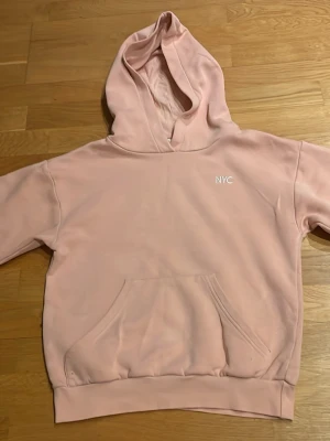 Rosa hoodie med liten text på - Säljer denna rosa hoodie med liten vit broderad text på. Hoodien ser bra ut på utsidan men på insidan av tröjan ser man att den har varit använd . Storlek 146/152 från H&M. 