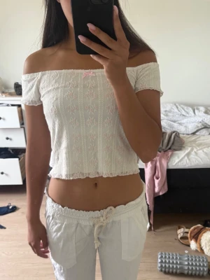 Vit offshoulder vintage topp - Säljer en söt vit offshoulder blus med ljusrosa broderade detaljer och liten rosett framtill. Toppen är croppad och har en romantisk vibe med spets och vågig kant. Perfekt för sommarens alla tillfällen! Den är en L i storlek men passar allt ifrån xs till L, jag är en S.