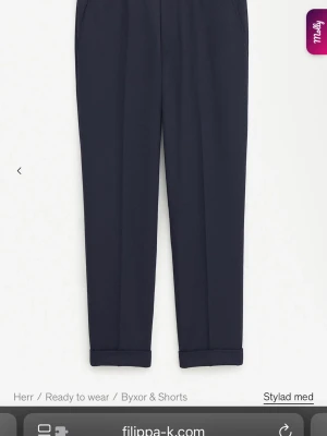 Mörkblå kostymbyxor från Filippa K - Snygga mörkblå kostymbyxor från Filippa K med elastisk midja och uppvikta benslut. Byxorna har en rak passform och är tillverkade i ett mjukt material som ger en clean och stilren look. Perfekta för dig som gillar minimalistisk stil. Nypris 1700kr