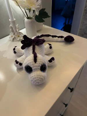 Vit drake med lila detaljer🤍💜 - Denna söta drake letar efter sitt nya framtida hem💜🤍🐉 Denna är virkad med kärlek, jag älskar att virka💜 Den är virkad av mjukt garn från Rusta, hårda ögon som inte går att ta av. Den är 54cm lång och man sträcker ut svansen🐉