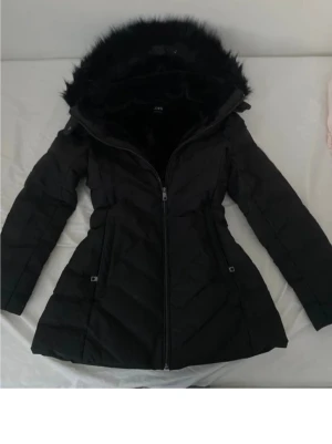 Svart pufferjacka från Zara med fuskpäls - Säljer en svart pufferjacka från Zara med stor huva kantad av mjuk fuskpäls. Den är nevöns men är ändå i bra skick