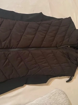 Svart quiltad dunväst från Zara - Säljer en svart dunväst från Zara i storlek L. Västen är nog ganska stretchig så den passar perfekt om man har storlek M. Västen har ett quiltat mönster med snedställda sömmar och dragkedja framtill. Perfekt att slänga över en hoodie eller tröja när det är lite kyligt ute. Stilren och enkel design som funkar till många outfits.
