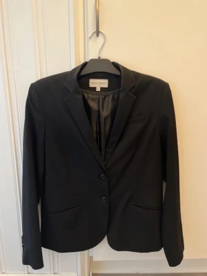 Svart kavaj från KappAhl - Säljer en klassisk svart kavaj från Dewply KappAhl. Kavajen har två knappar framtill, fickor i sidan och på bröstet och fyra dekorativa knappar vid ärmsluten. Snygg passform och helfodrad insida. Använd några gånger men är i fint skick! 