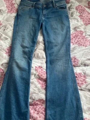 Blå bootcut jeans från Pepe Jeans - Säljer ett par ljusblå pepe jeans. De är i super bra skick då de bara andvändts några gånger. De är lowwaist fast det står mid waist. De sitter långt under naveln. Storlek 27 men de passar 26! Jag brukar ha 26 men de passar toppen 🫰