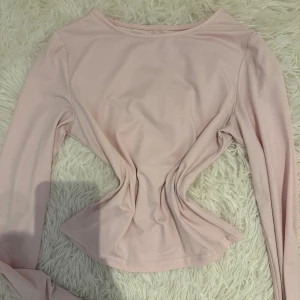 Ljusrosa långärmad topp - Säljer en ljusrosa långärmad topp med rund halsringning. Toppen har en enkel och stilren design med figurnära passform och är tillverkad i mjukt bomullsmaterial. Perfekt att matcha med jeans eller kjol för en clean look.