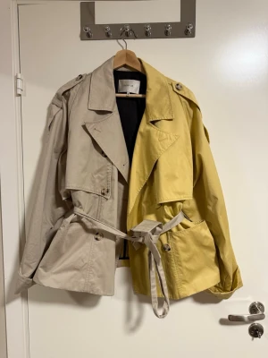 Tvåfärgad kort trenchcoat från Gestuz - Unik kort trenchcoat från Gestuz i beige och gul. Storlek M/L men skulle söga att den passar äcen S lite oversized❣️Superfin till våren💘 nypris ca 3000kr, buda gärna💘
