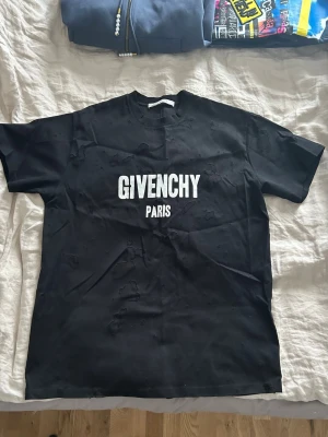 Givenchy t-shirt svart - Svart t-shirt från Givenchy med stor vit logotyp 'GIVENCHY PARIS' på bröstet. T-shirten har cool distressed look med små hål och slitningar över hela plagget. Materialet är 100% bomull med detaljer i polyester. T-shirten är storlek XS men är en oversize modell så kan passa folk med S/M. Säljer då den samlar bara damm. Nästintill nytt skick då jag använt 4-5 gånger. ÄKTA