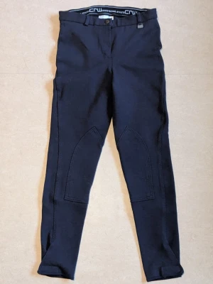 RIDBYXOR CRW, 38 - HELT OANVÄNDA RIDBYXOR. Mörkblå ridbyxor från CRW. De har en klassisk design och förstärkta partier på insidan av benen för extra komfort vid ridning. Längst ner på byxbenen kardborre. RIDBYXORNA ÄR HELT OANVÄNDA. Jag har inte prislappen kvar på ridbyxorna och original förpackningen har jag inte heller kvar som ridbyxorna låg i när dem köptes