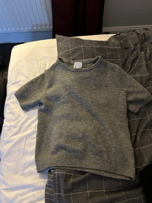 Grå stickad kortärmad tröja H&M - Mysig grå stickad tröja från H&M i storlek S. Tröjan har korta ärmar, rund halsringning och ribbade kanter. Perfekt för lager på lager under höst och vår. Enkel och stilren design som passar till det mesta.
