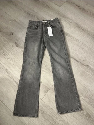 Grå flare jeans från Perfect Jeans - Säljer ett par gråa full length petite flare jeans från Perfect Jeans i storlek 34. Klassisk femficksmodell med hög midja och utsvängda ben. Jeansen är i mjuk denim och har en snygg tvättad look. Perfekta för dig som gillar retrovibbar och vill ha en trendig siluett.