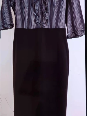 Svart långkjol med randig topp - Snygg svart långkjol med rak passform och hög midja. Kjolen har en randig toppdel i svart och vitt med knappar och volangdetaljer framtill. Perfekt för dig som gillar en stilren och klassisk look.