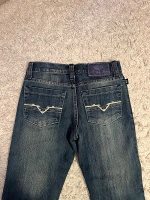 Victoria Beckham x Rock & Republic jeans - Mörkblå jeans med snyggt slitna detaljer och kontrastsömmar. Bakfickorna har broderad logga i vitt och jeansen har klassisk femficksdesign. Märke: Victoria Beckham x Rock & Republic. Perfekta för dig som gillar stilrena och coola jeans. Säljer pga av att dom tyvär är lite för små för mig.💞