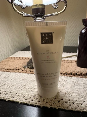 Rituals The Ritual of Sakura body cream - Testad. Rituals The Ritual of Sakura Magic Touch Body Cream i en vit tub på 70 ml. Innehåller risextrakt och körsbärsblomma för en lyxig och återfuktande känsla. Tuben har elegant design med guldiga detaljer och text på engelska och franska.