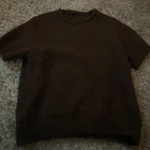Mörkbrun stickad kortärmad tröja - Säljer en mörkbrun stickad tröja med korta ärmar och rund hals. Tröjan har en enkel och clean design utan mönster eller detaljer, perfekt för dig som gillar basic och comfy vibes. Materialet är mjukt och ger en mysig känsla.