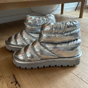 Silvriga boots i storlek 36 - Säljer ett par riktigt coola silvriga boots med quiltad design och chunky sula. Skorna har en glansig metallic finish och är vadderade för extra komfort. Perfekta för dig som vill sticka ut under vintern och hålla fötterna varma.