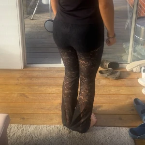 Svarta spetsbyxor med bootcut - Säljer ett par svarta byxor i genombruten spets med blommigt mönster. Byxorna har bootcut och sitter snyggt i midjan. Perfekta för dig som vill sticka ut med en cool och trendig look. Spetsen ger en extra touch och de är riktigt bekväma.