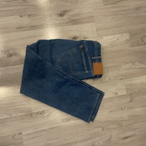 Lee Daren Zip Fly jeans blå W36 L32 - Snygga blå Lee Daren Zip Fly jeans med klassisk femficksdesign och brunt läderpatch bak. Jeansen har raka ben och gul kontrastsöm, tillverkade i slitstarkt bomullsjeansmaterial. Perfekt passform och stilren look.