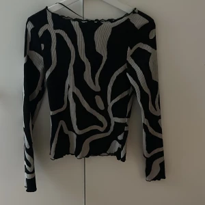 Zebramönstrad topp från AWARE XS - Säljer en långärmad topp från AWARE i storlek XS med svart och grått zebramönster. Toppen är ribbad och har vågig kant vid halsringningen och nederkanten. Perfekt för dig som gillar att sticka ut med coola mönster.