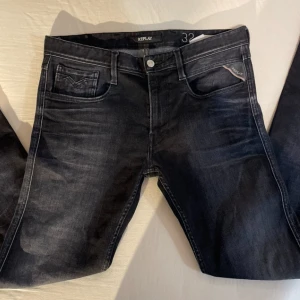 svarta replay jeans - Snygga svarta jeans från Replay med diskret tvättad look och klassiska fem fickor. Jeansen har slim passform och silverfärgade detaljer vid knappar och nitar. Perfekta för dig som gillar stilrena och moderna jeans.