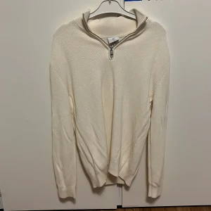 Vit stickad half zip-tröja H&M - Vit stickad tröja från H&M med half zip-dragkedja och hög krage. Slim fit-modell med ribbade detaljer på axlar och ärmslut. Perfekt för lager-på-lager och snygg till både jeans och chinos.