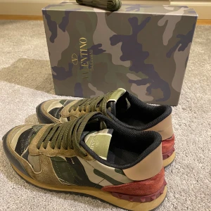 Valentino Rockrunner  - Säljer ett par Valentino Rockrunner sneakers med camouflagemönster i grönt, beige och svart. Skorna har detaljer i mocka och skinn, samt röda partier med nitar på hälen. Platt sula och rund tå, med gröna snören och svart meshfoder. Box medföljer. Storlek 40 men sitter som 41
