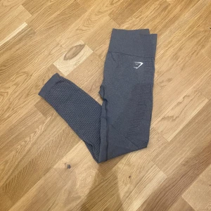 Träningstights från Gymshark - Snygga mörkgrå leggings från Gymshark med hög midja och ventilerande mesh-detaljer längs benen. Stretchigt syntetmaterial som sitter tight och följer kroppens rörelser. Perfekta för gymmet eller andra träningspass.