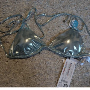 Glittrig blå bikini - Supersnygg glittrig blå bikiniöverdel i trekantsmodell med tunna snören att knyta i nacken och ryggen. Materialet är syntet och har en metallic finish som verkligen poppar. Perfekt för dig som vill sticka ut på stranden!