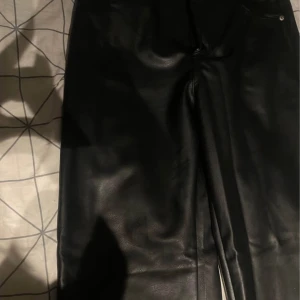 Svarta skinnbyxor från H&M, strl 40 - Snygga svarta byxor i skinnimitation från H&M. Klassisk femficksmodell med knapp och dragkedja framtill. Byxorna har en rak passform och är perfekta för att lyfta vilken outfit som helst.