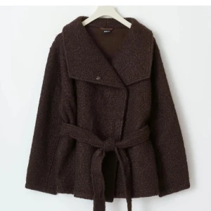 Mörkbrun teddyjacka med bälte - Säljer en mörkbrun teddyjacka från Gina med bred krage och knytbälte i midjan. Jackan har lång ärm och en oversized, loose passform som ger en chill vibe. Materialet är mjukt och fluffigt, perfekt för kalla dagar. Enkel knappstängning framtill.