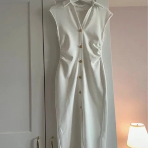 Vit ärmlös klänning med guldknappar - Högst bud 303kr Lyxigt tyg. Passar även XS. Supersnygg vit klänning från ZARA med krage, v-ringning och dekorativa guldknappar framtill. Klänningen är ärmlös och har en rak, figurnära passform som slutar under knäet. Perfekt för dig som gillar stilrena och eleganta plagg.