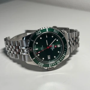 Swiss Military by Chrono Verbier - Till salu en otroligt fin sport klocka. Låda och kvitto finns!  Info:  Ref - SM34109.03 Produkttyp - Analog Stil - Sportklocka Boettstorlek - 42 mm Tjocklek - 11,30 mm Boettmaterial - Stål Boettfärg - Silver Material Armband/länk - Stål Färg armband/länk - Silver Färg Urtavla - Grön Glas, ur/klocka - Safir Urverk - Quartz  Kaliber - Ronda 515 Vattentäthet - 10 ATM Sekundvisare - Tickande Datumangivelse - Datum Varumärke - Swiss Military By Chrono